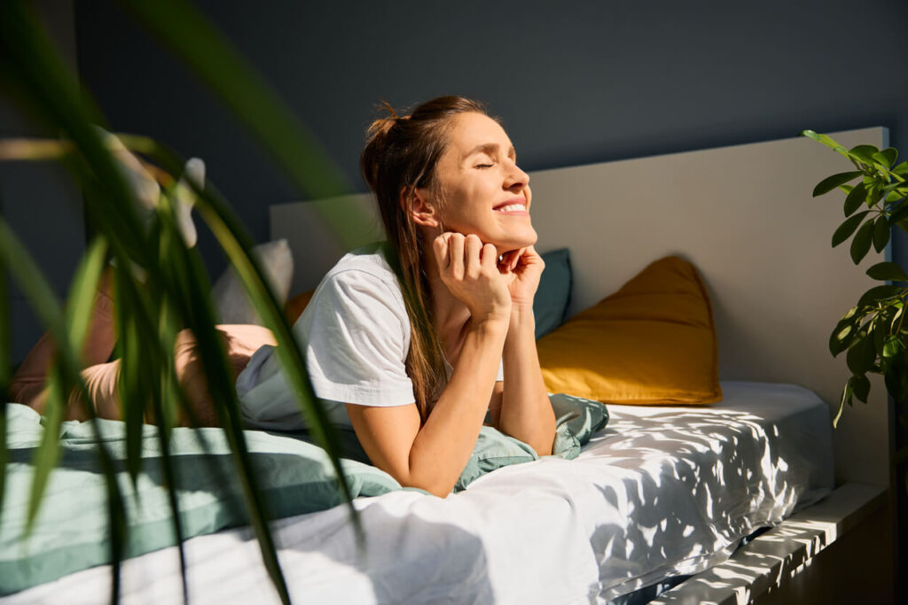 Woman enjoying daylight lying on bed at home